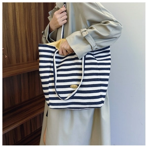 Detail of navy stripe canvas tote bag with Handmade tag carried by a model in a trench coat