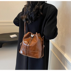 Sac seau marron brillant avec boucle nœud porté sur un manteau noir dans un décor élégant