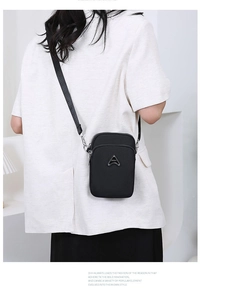 Detail of black nylon crossbody phone bag with double zippers and metal logo on a model