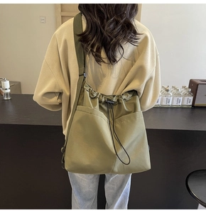 Model wearing large olive green nylon crossbody bucket bag with drawstring closure