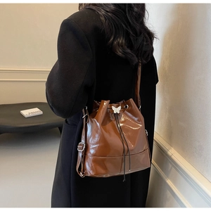 Détail d'un sac seau en cuir marron brillant avec un charme de cordon papillon blanc