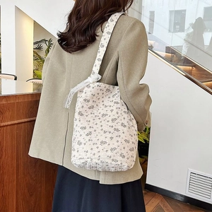 Floral print canvas hobo bag with lace bow shoulder strap in a minimalist indoor setting