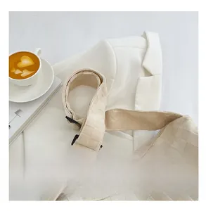 Detail showing the adjustable wide shoulder strap and buckle of the beige checkerboard bag