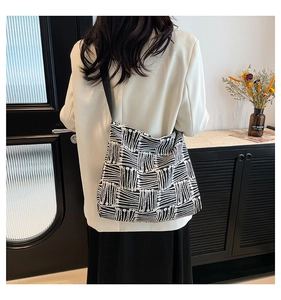 Rear view of a large black and white striped tote bag worn by a model in a modern room
