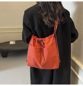 Detail view of bright orange drawstring bucket bag with dual front pockets and long strap