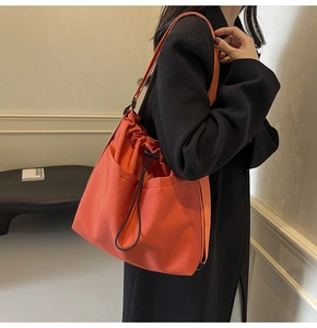 Detail of orange drawstring tote bag made of nylon fabric worn with a black wool coat