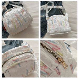 Détails d'un sac bandoulière blanc avec broderies multicolores et texture en tissu gaufré