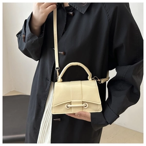 Minimalist cream shoulder bag with stylish latch detail on black coat background