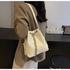 Détail d'un sac seau blanc cassé avec fermeture à cordon et pendentif papillon argenté poli