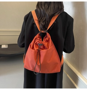 Detail of orange nylon drawstring bucket bag on model with black suit for streetwear style
