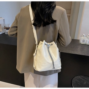 Détail d'un sac seau crème avec fermeture à cordon et breloque papillon dans un cadre de café