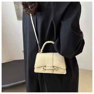 Detail of cream crossbody bag featuring trapezoid shape and matching handle strap