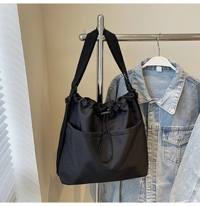 Detail of black drawstring bucket bag with dual front pockets and wide webbing strap