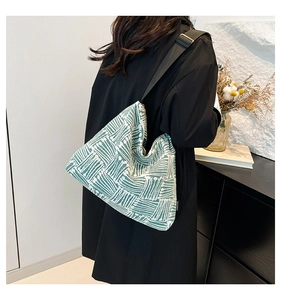 Detail of green and white woven tote bag featuring adjustable black nylon strap on a model