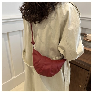 Détail d'un sac croissant rouge foncé porté sur un manteau beige pour un look d'automne