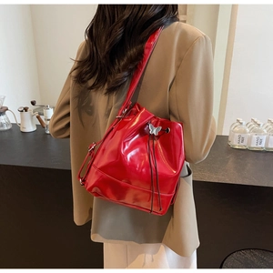 Détail du sac seau en cuir verni rouge avec boucle papillon argentée porté par un mannequin