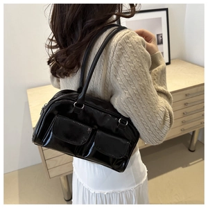 Détail d'un sac Boston noir brillant avec poches avant porté par un mannequin en salle