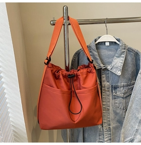 Detail view of an orange drawstring bucket bag with dual front pockets and wide strap