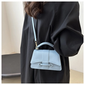 Close-up of a light blue crossbody bag with unique buckle detail worn on a black outfit