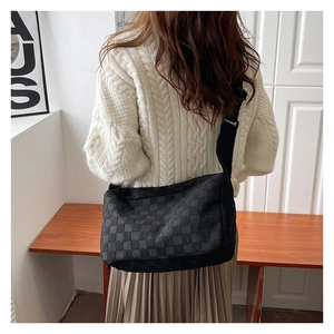Detail view of black woven checkerboard crossbody bag with adjustable wide shoulder strap