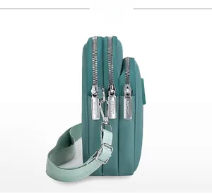 Detail view of teal nylon crossbody phone bag with three layered silver zipper compartments