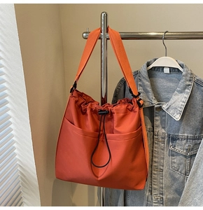 Detail of orange drawstring bucket bag with double front pockets and wide fabric strap