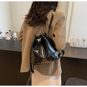 Détail d'un sac seau noir brillant avec breloque papillon argentée et fermeture à cordon