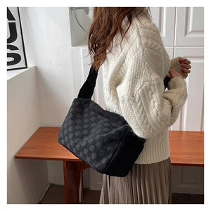 Detail showing the thick textured woven fabric and soft black grid pattern of the shoulder bag
