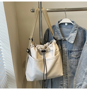 Detail of cream drawstring bucket bag featuring front pockets and wide shoulder strap
