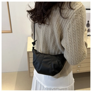Détail du sac croissant noir avec coutures plissées sur tenue de pull beige