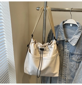 Detail of minimalist cream drawstring bucket bag with large front pockets and nylon strap