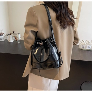 Sac seau en cuir noir avec fermoir papillon et cordon, porté comme un sac à bandoulière