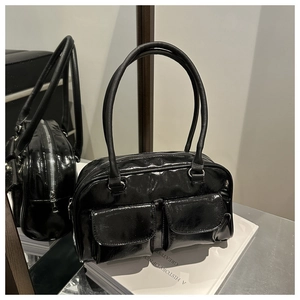 Détail d'un sac à bandoulière en cuir verni noir avec deux poches avant et une finition brillante