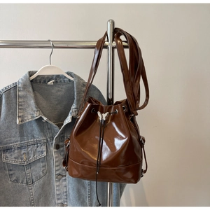 Détail d'un sac seau en cuir verni marron avec fermoir papillon argenté sur fond en jean
