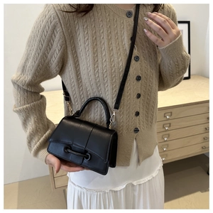 Classic black crossbody bag with smooth texture and decorative buckle on a model
