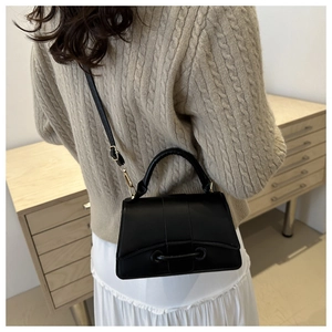 Crossbody view of the black textured small square bag with flap and metal buckle detail