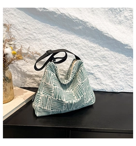 Detail of woven tote bag with green geometric stripes and adjustable black shoulder strap