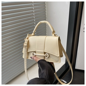 Detail view of cream-colored crossbody bag with unique metal buckle and smooth PU leather
