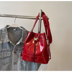 Détail du sac seau en cuir verni rouge avec boucle papillon argentée et cordon de serrage
