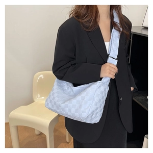 Detail of light blue woven crossbody bag worn by model over a black blazer jacket