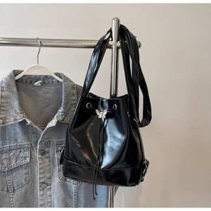 Détail du sac seau noir brillant avec breloque papillon argentée sur un cintre