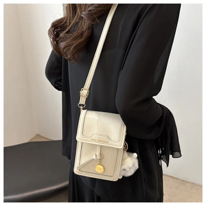 Dettaglio borsa a tracolla beige con ciondolo dorato e morbido pompon bianco