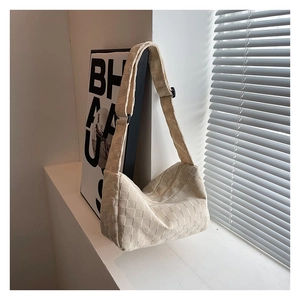 Detail of off-white woven hobo bag showing textured fabric and adjustable strap on window sill