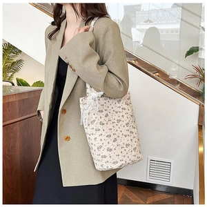 Detail of floral bucket bag with lace bow accessory held by a model in green blazer
