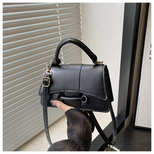 Detail of black minimalist square handbag with pleated handle and metal bar closure