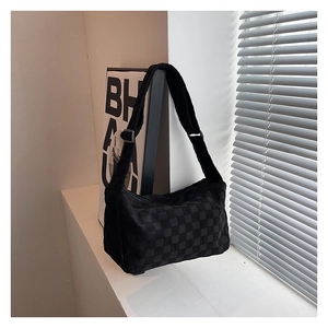 Close-up of black checkerboard textured suede bag with wide adjustable shoulder strap