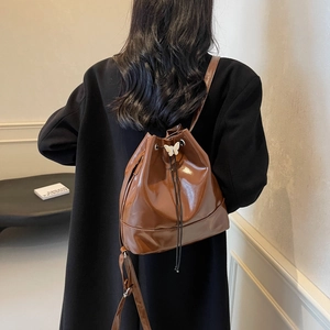 Sac seau marron brillant avec boucle papillon argentée porté par un mannequin en intérieur