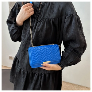 Close-up of royal blue quilted chain bag with gold metal lock on a black dress