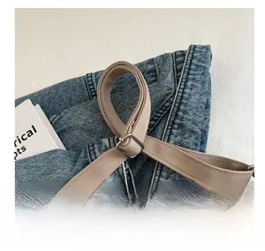 Close-up of washed blue denim bag featuring beige woven strap and silver metal buckle