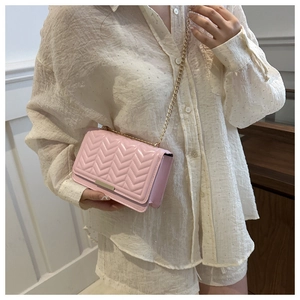 Detail of pink quilted crossbody bag with gold chain strap worn by a female model
